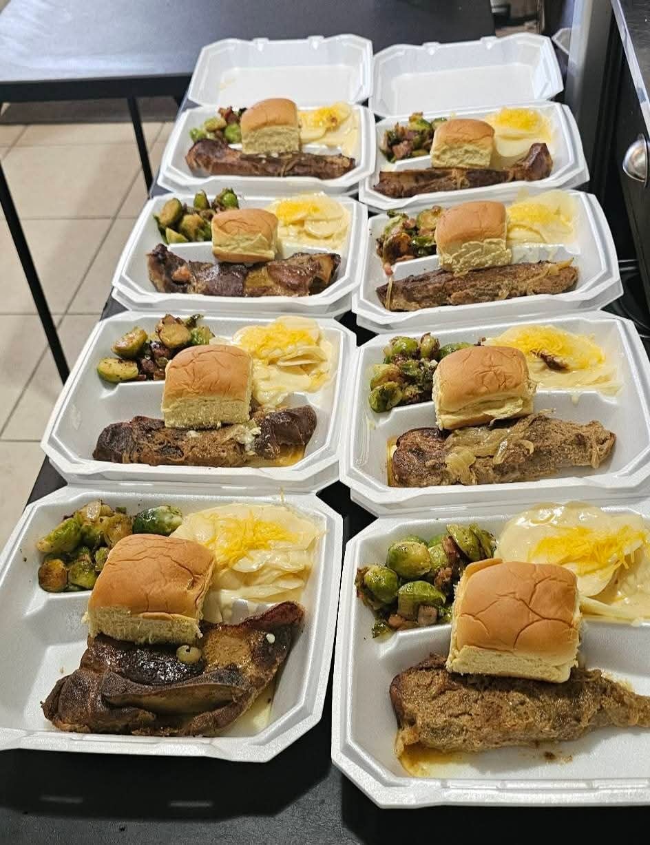 Smothered ribs and brisket to-go trays with baked rolls, scalloped potatoes, and Brussels sprouts